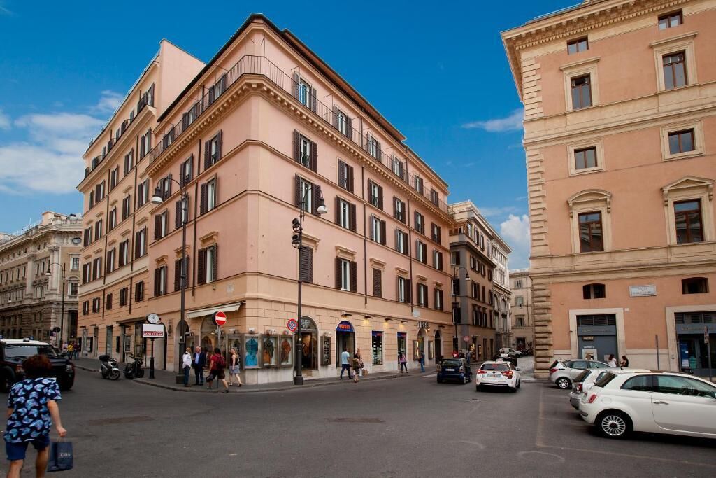 Hotel de vários andares com arquitetura clássica, apresentando uma entrada de canto e um andar térreo visível com lojas.