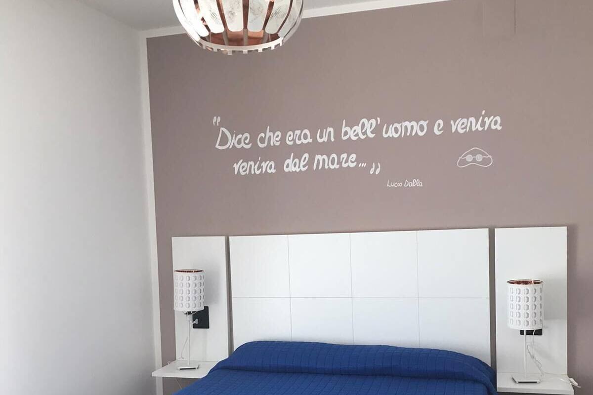 A modern bedroom with a large bed, a decorative wall quote, and bedside lamps.