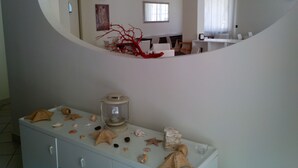 A modern room with a curved mirror reflecting a dining area, a white cabinet with seashells, and a red decorative piece. - Hotel Sette Note (Silvi)