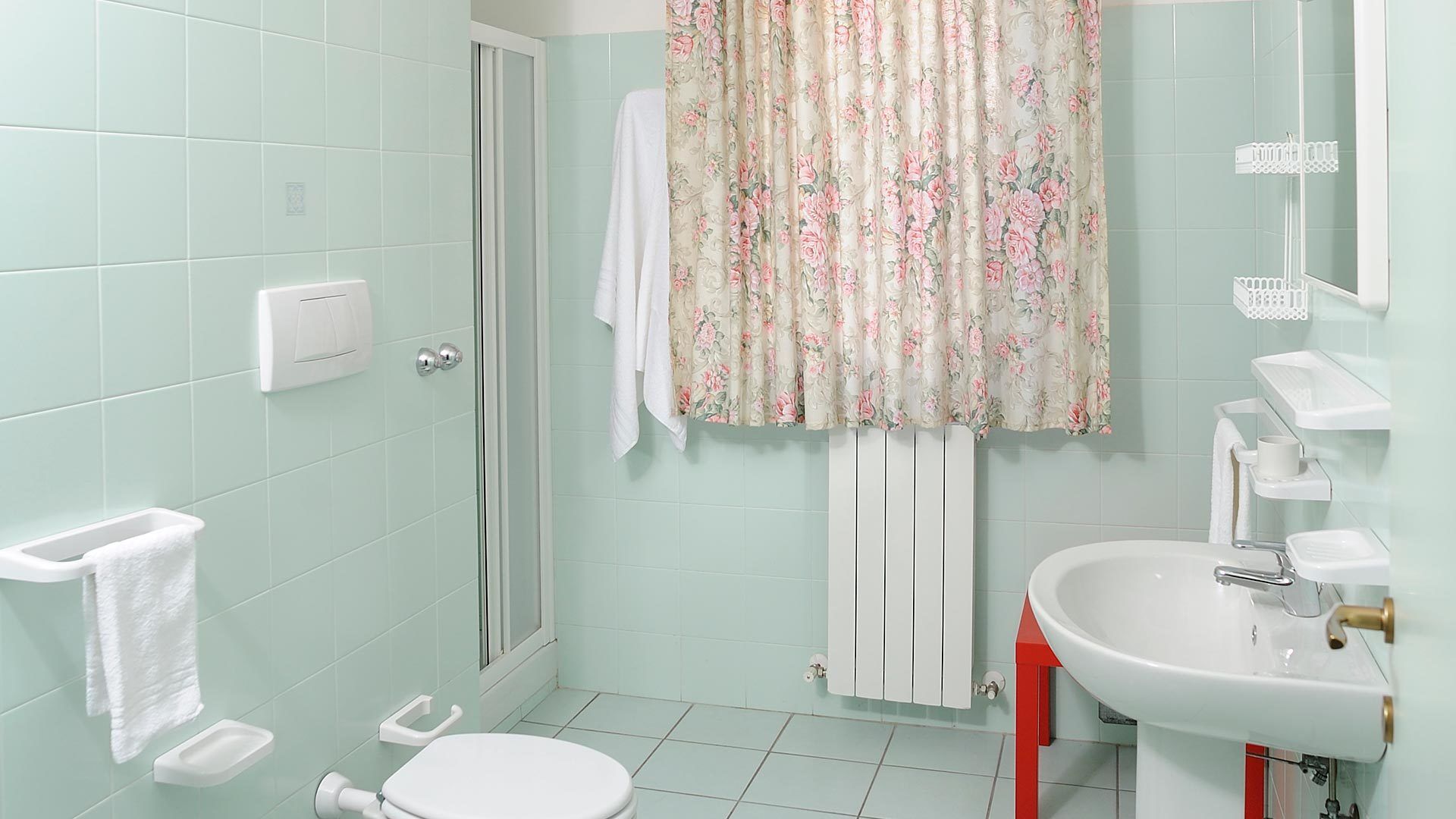 A bathroom with a toilet, shower, sink, and a towel rack.
