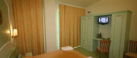 A hotel room with a bed, a television on a cabinet, a chair, and a desk.