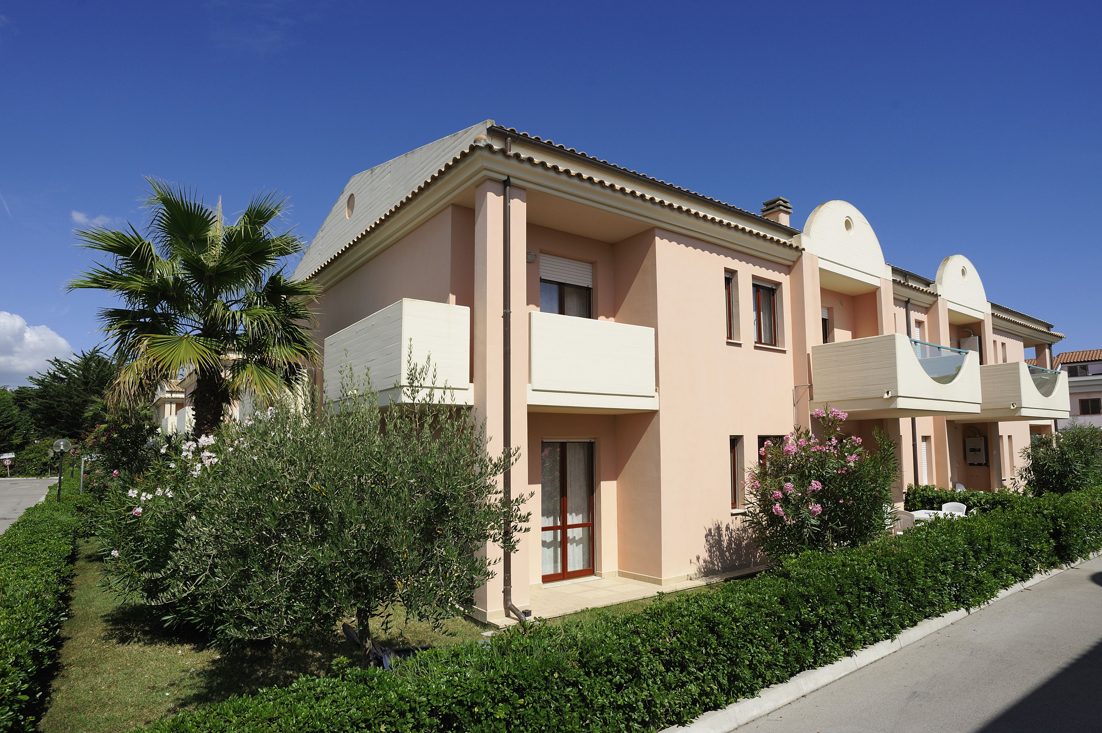 A two-story building with a flat roof, a balcony on the second floor, and a small porch area.