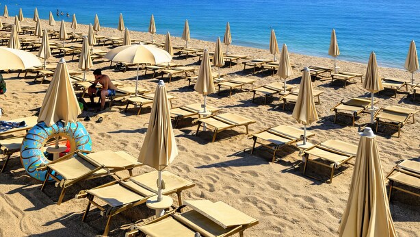A beach with rows of sun loungers and umbrellas, a clear blue sky, and a boat in the water. - Centro Vacanze De Angelis (Numana)