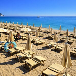 A beach with rows of sun loungers and umbrellas, a clear blue sky, and a boat in the water. - Centro Vacanze De Angelis (Numana)