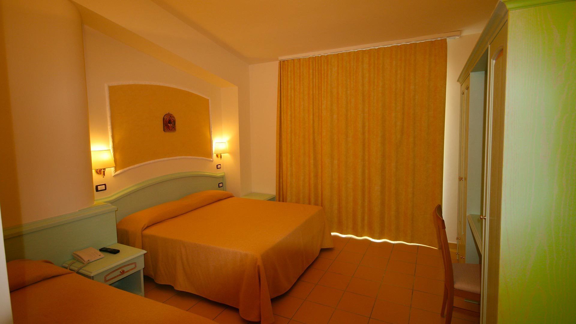 A hotel room with a bed, bedside table, lamp, and a curtain.
