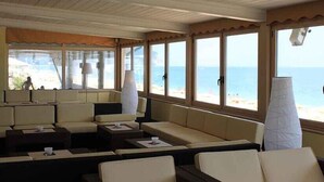 A sunlit room with a view of the beach, featuring a sofa area, tables, and large windows. - Centro Vacanze De Angelis (Numana)