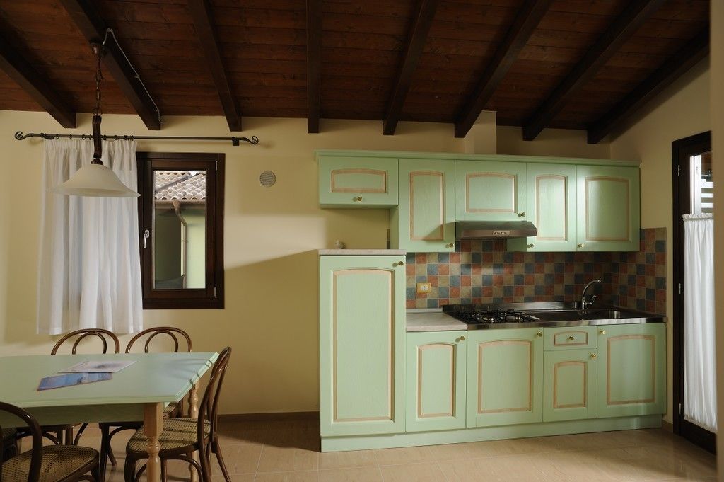 A kitchen with light green cabinets, a tiled backsplash, and a wooden ceiling.