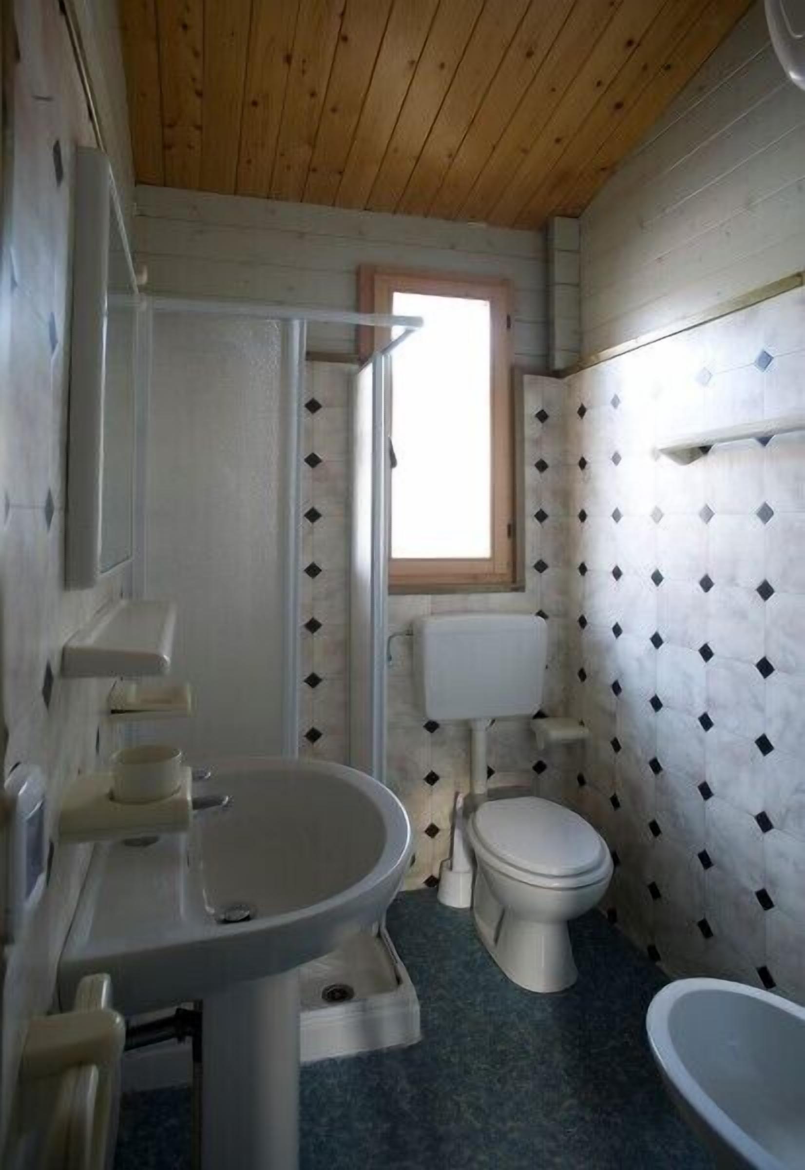 A compact bathroom with a wooden ceiling, a toilet, a sink, and a window.