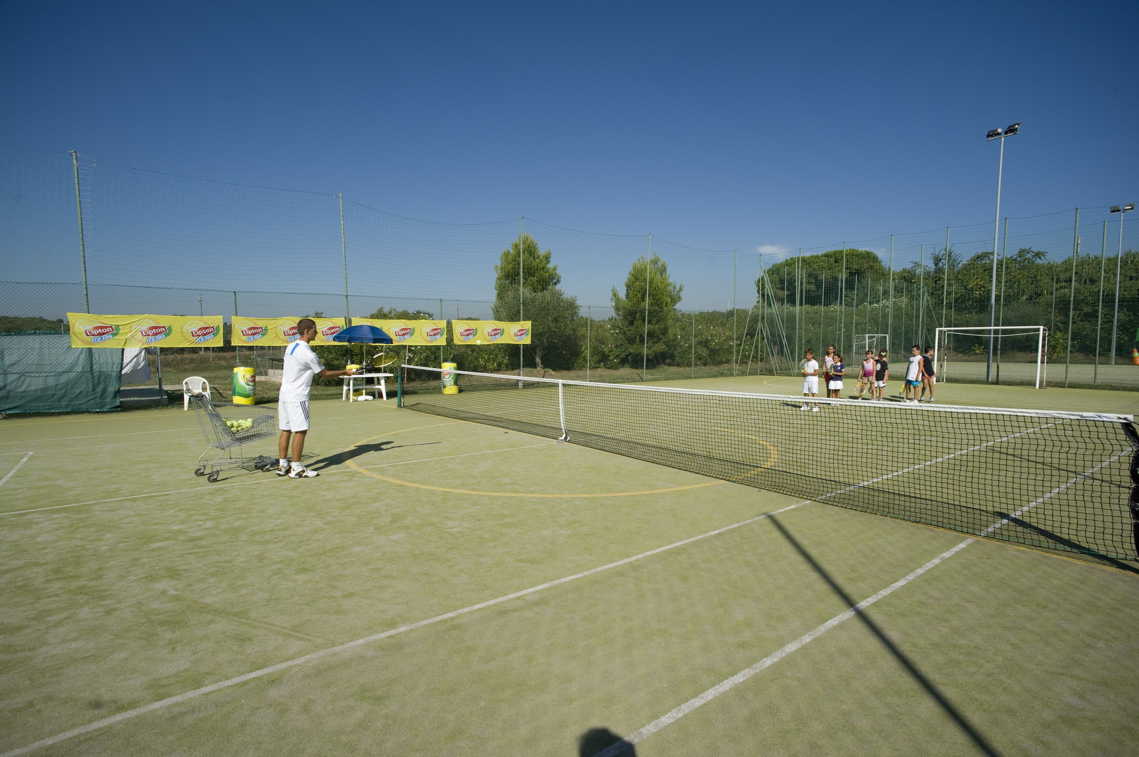 An outdoor tennis court with a net, a goalpost, and a few people.