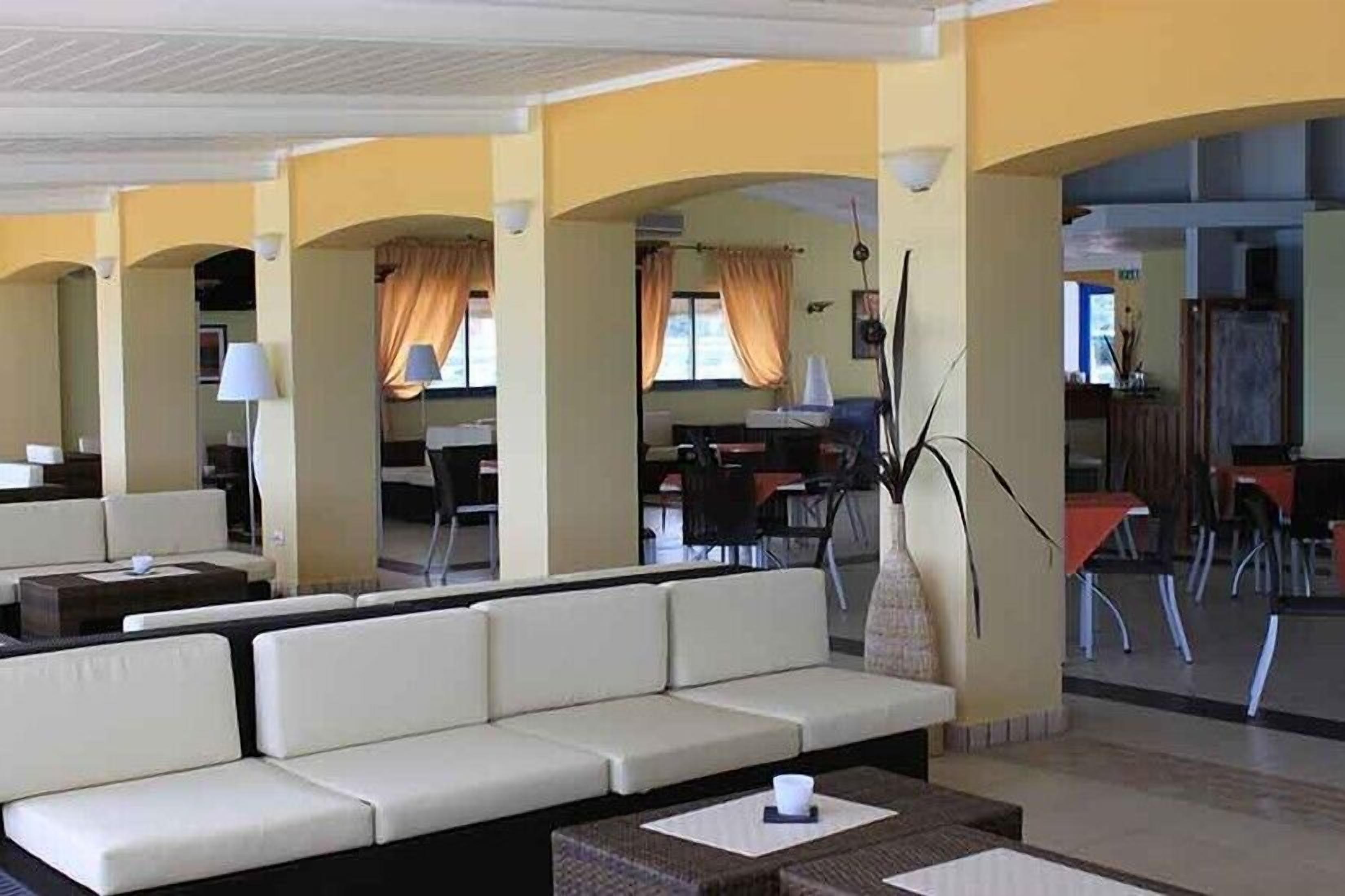 A hotel lobby with a seating area, a dining area, and a reception desk.