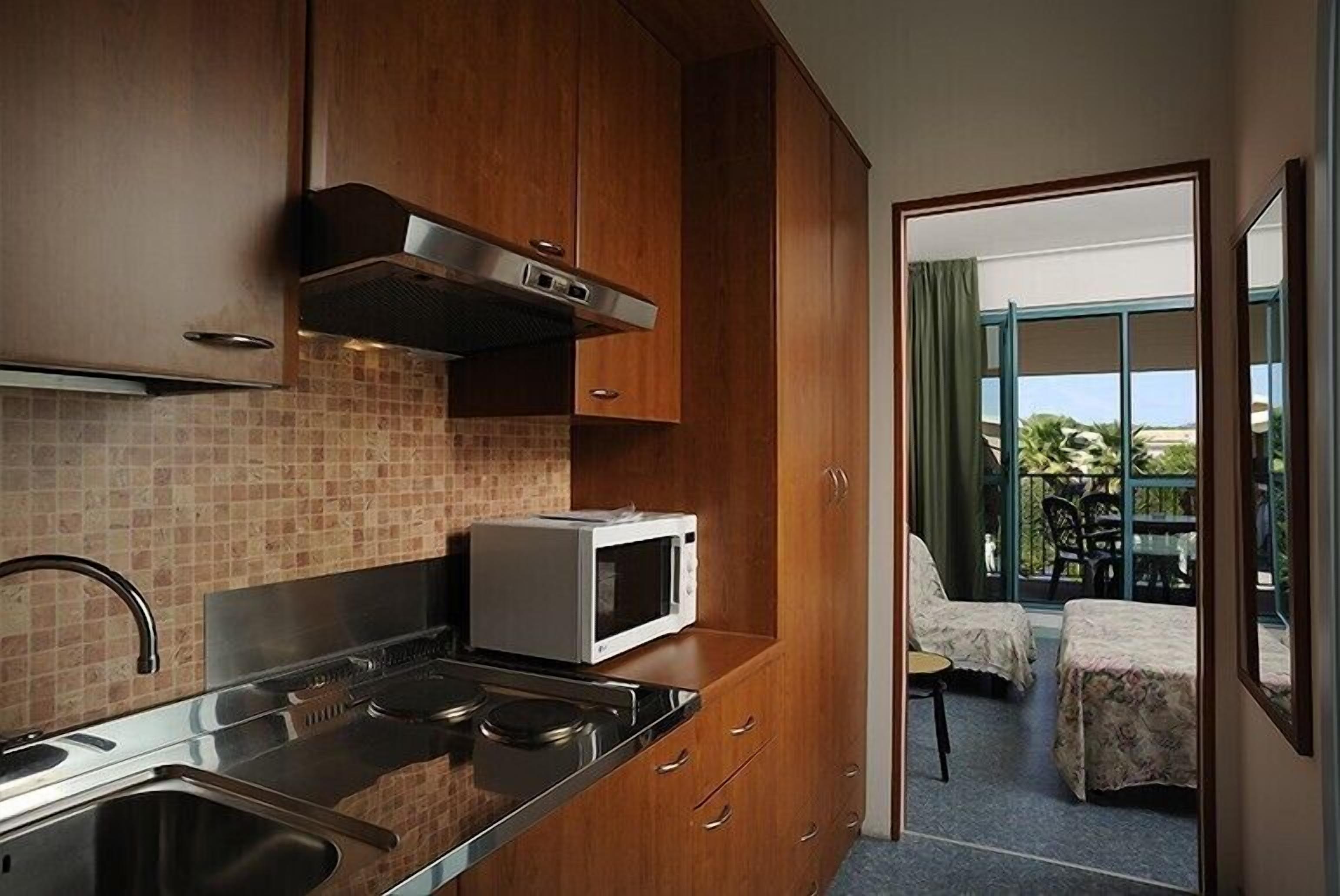 Eine kleine Küche mit Mikrowelle, Herd und Spüle. Durch eine offene Tür ist ein Balkon mit Tisch und Stühlen zu sehen.