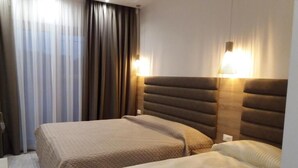 Habitación de hotel con dos camas, un ventanal grande con cortinas y lámparas fijadas a la pared.