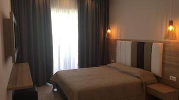 A modern hotel room with a large bed, a bedside table, a nightstand, and a window with curtains.