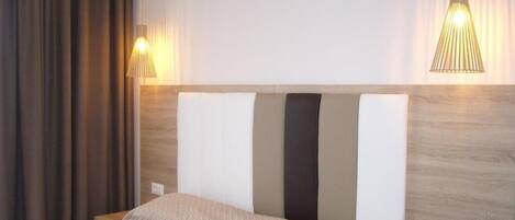 A hotel room with a bed, a headboard with vertical stripes, and two pendant lights.
