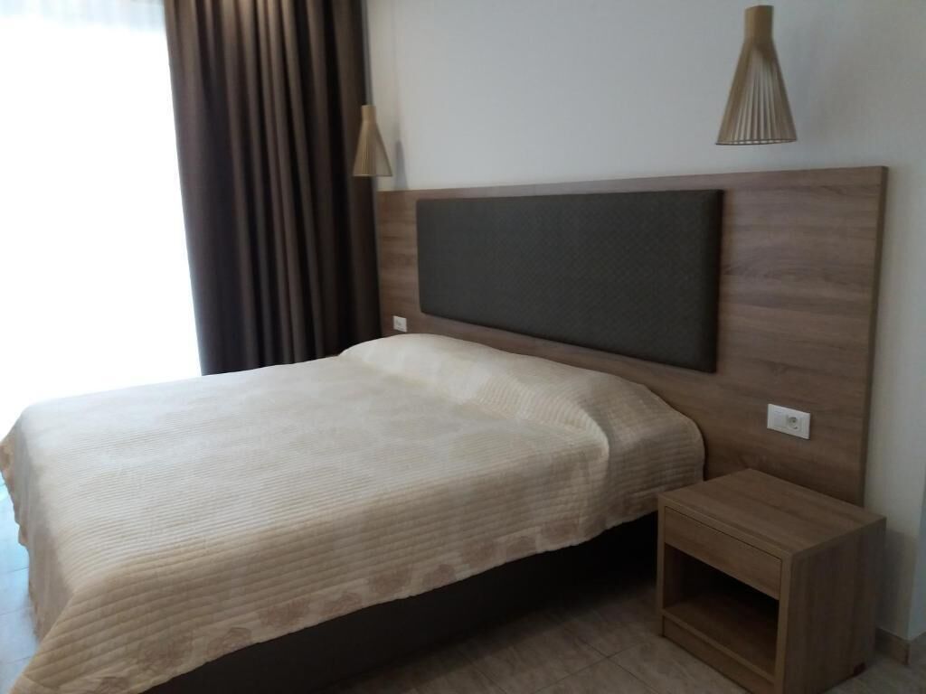 A neatly made bed with a headboard, a bedside table, and a lamp on the wall.