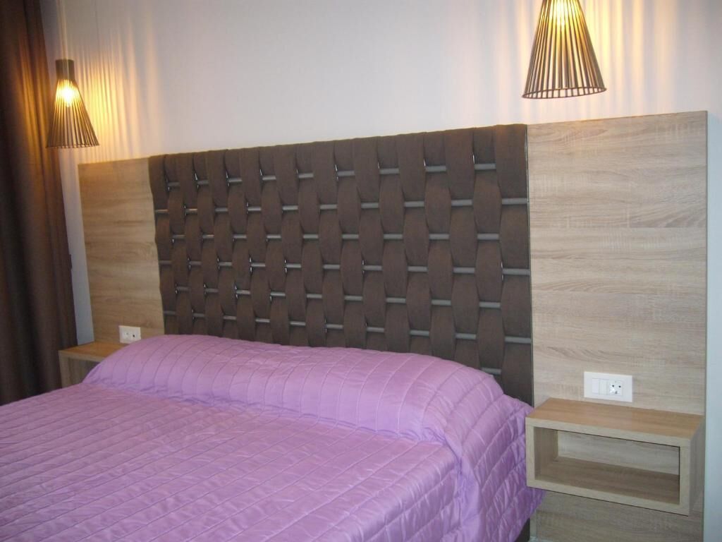 Een slaapkamer met een gestapeld hoofdbord, een paars sprei, twee bedlampen en een houten nachtkastje.