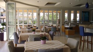 Un restaurante con mesas cubiertas por manteles a cuadros, sillas con tapicería estampada y plantas en macetas.