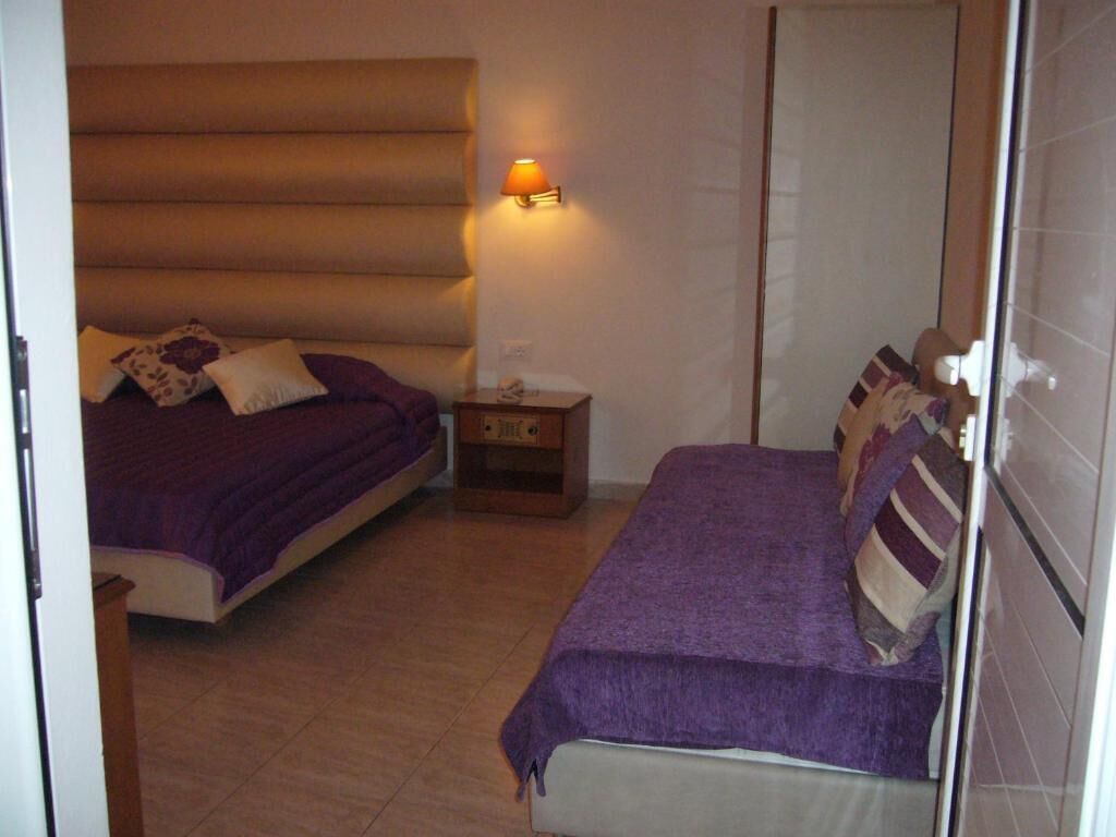 A bedroom with two beds, a nightstand, and a wall-mounted lamp.