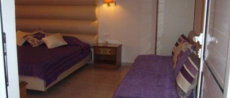 A bedroom with two beds, a nightstand, and a wall-mounted lamp.