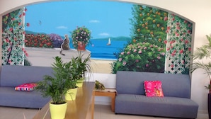 Una sala de estar con un gran mural de una escena de playa, dos sofás grises con cojines de colores, una mesa de centro de madera y plantas en macetas.