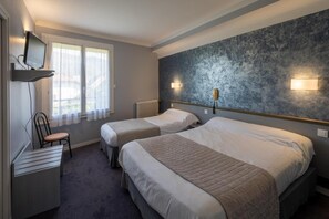 Una habitación de hotel con dos camas, un escritorio con silla, televisión y ventana con cortinas.