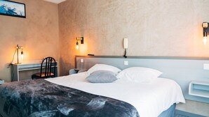 Habitación de hotel con cama, escritorio y silla. Hay luces fijadas a la pared y un televisor también en la pared.