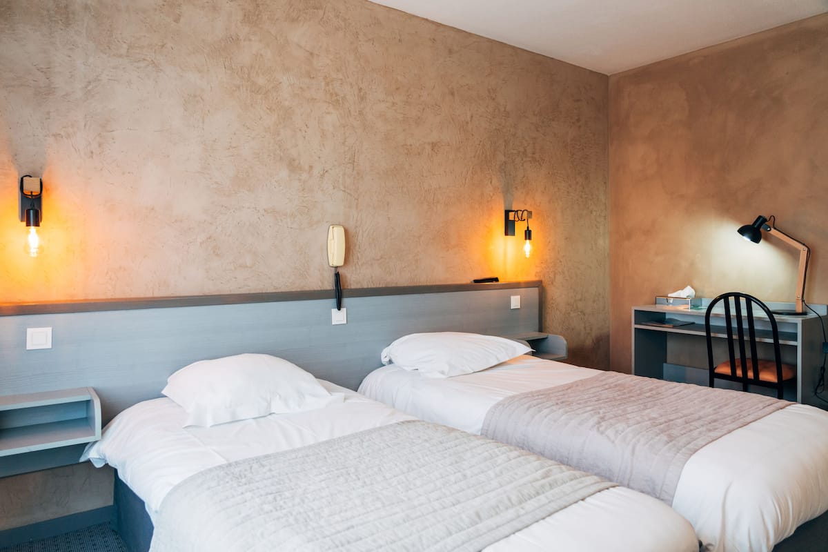 Ein Hotelzimmer mit zwei Betten, einem Schreibtisch, einem Stuhl und zwei Wandleuchten.