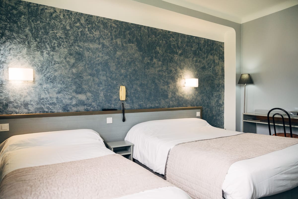 Ein Hotelzimmer mit zwei Betten, einem Nachttisch, einem Telefon, einem Schreibtisch mit Stuhl und einer Lampe.