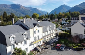 A hotel with a courtyard, multiple floors, and a mountain backdrop. - Hôtel du Soleil Levant (Argeles Gazost)