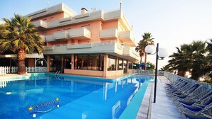 A swimming pool with lounge chairs, a building with balconies, and palm trees. - Residence Azzurro (Massignano)