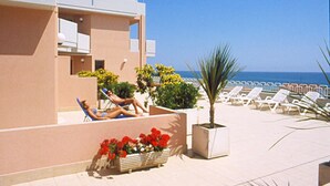 A poolside area with lounge chairs and a small garden with red flowers. - Residence Azzurro (Massignano)