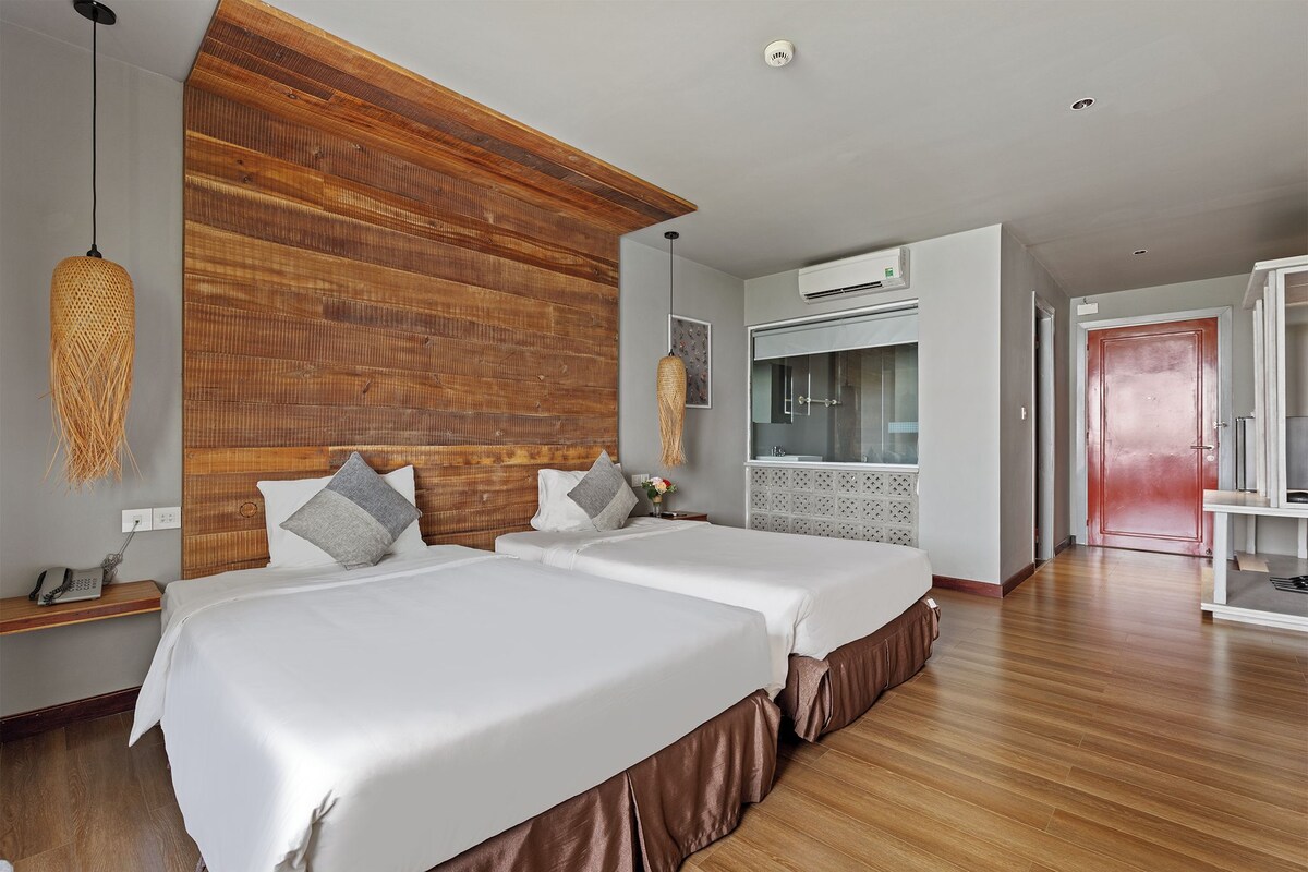 A hotel room with two beds, a wooden headboard, a hanging light fixture, an air conditioning unit, and a red door.