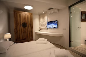Ein modernes Hotelzimmer mit einem großen Bett, einem an der Wand montierten Fernseher, einem Holzschrank und einer Duschkabine aus Glas.