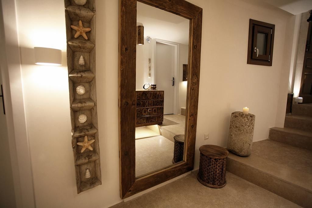 A hallway with a wooden door, a mirror, a stone wall decoration, a candle, and a small wooden stool.