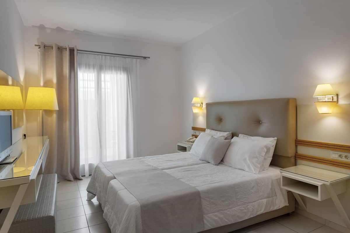 A hotel room with a bed, bedside tables, a desk with a lamp, and a TV.