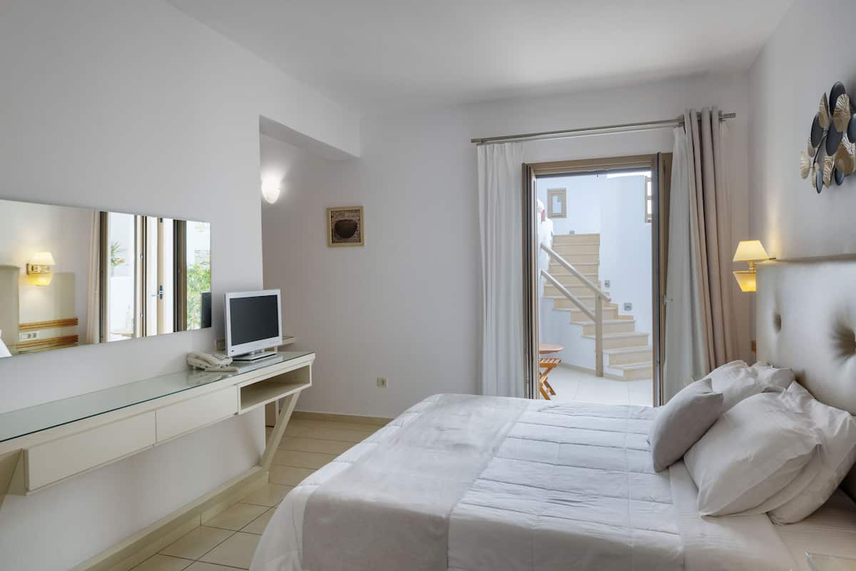 A bedroom with a bed, a desk with a computer, a mirror, and a staircase leading to an outdoor area.