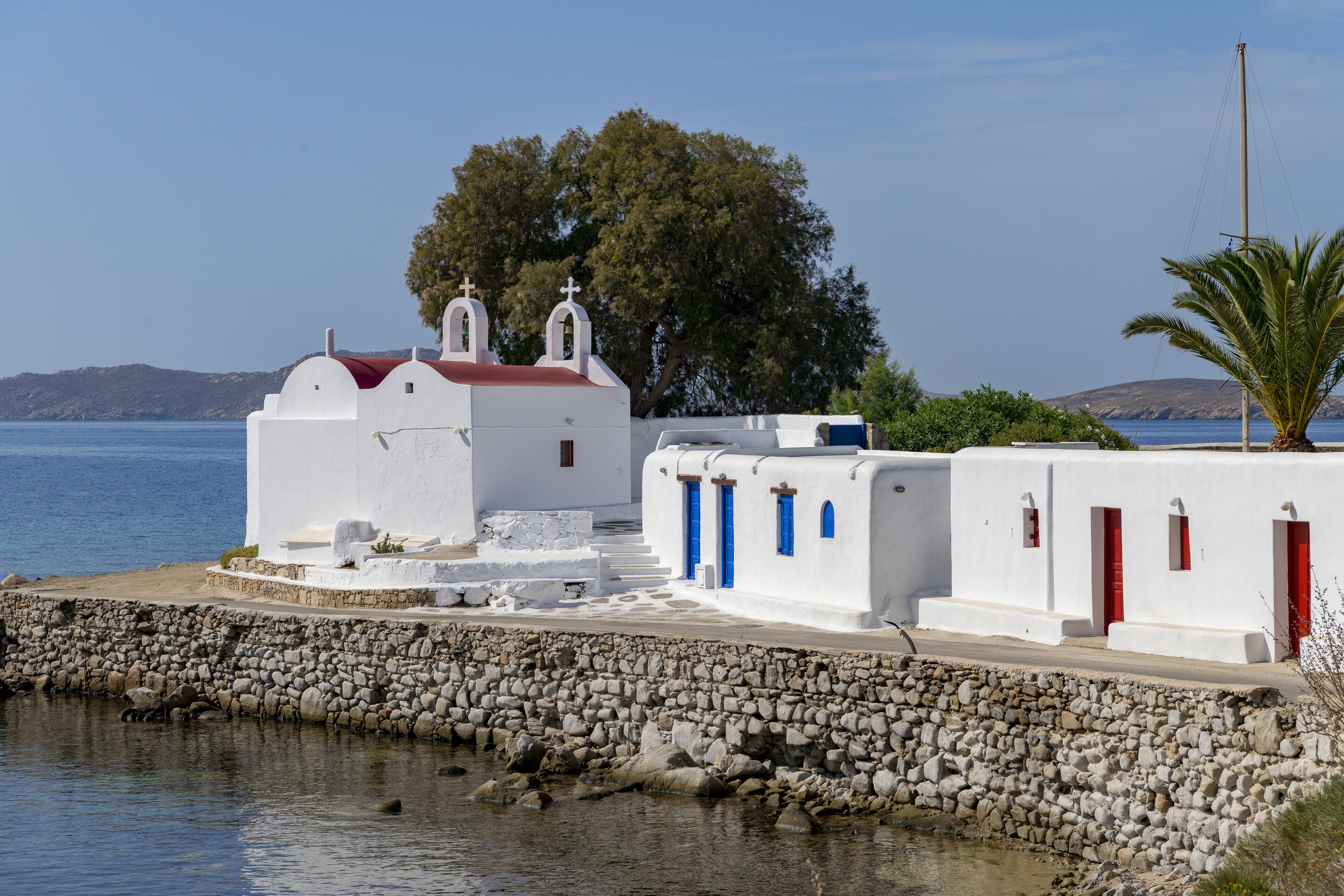 A white building with red doors and a stone wall by the water.