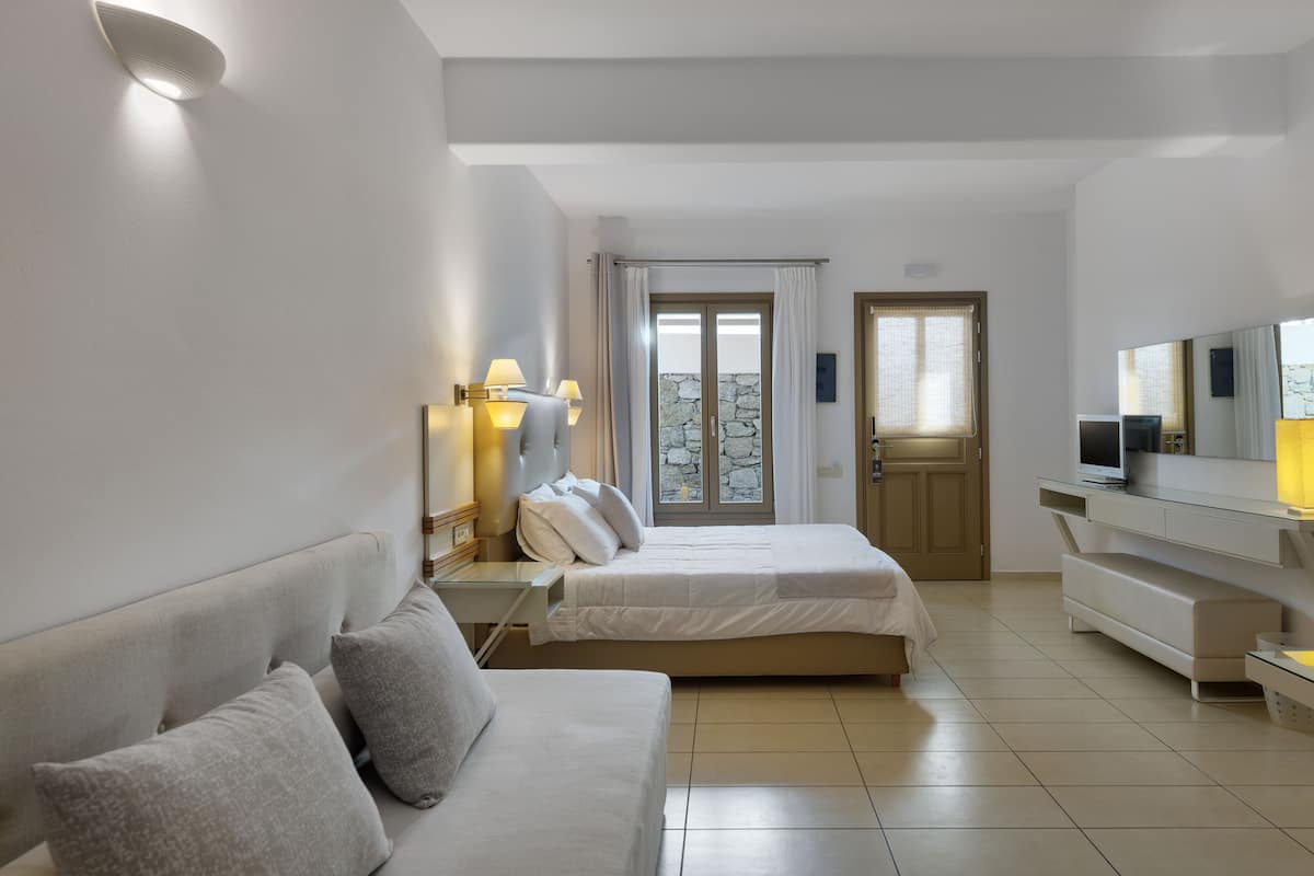 A modern hotel room with two beds, a sofa, a TV, and a balcony with a stone wall.