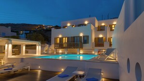 Um hotel moderno com piscina no terraço, espreguiçadeiras e área externa bem iluminada.