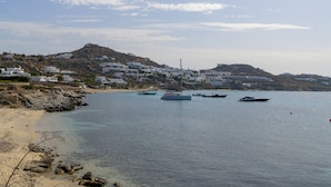 Uma vila costeira com edifícios brancos, uma praia de areia e barcos na água.