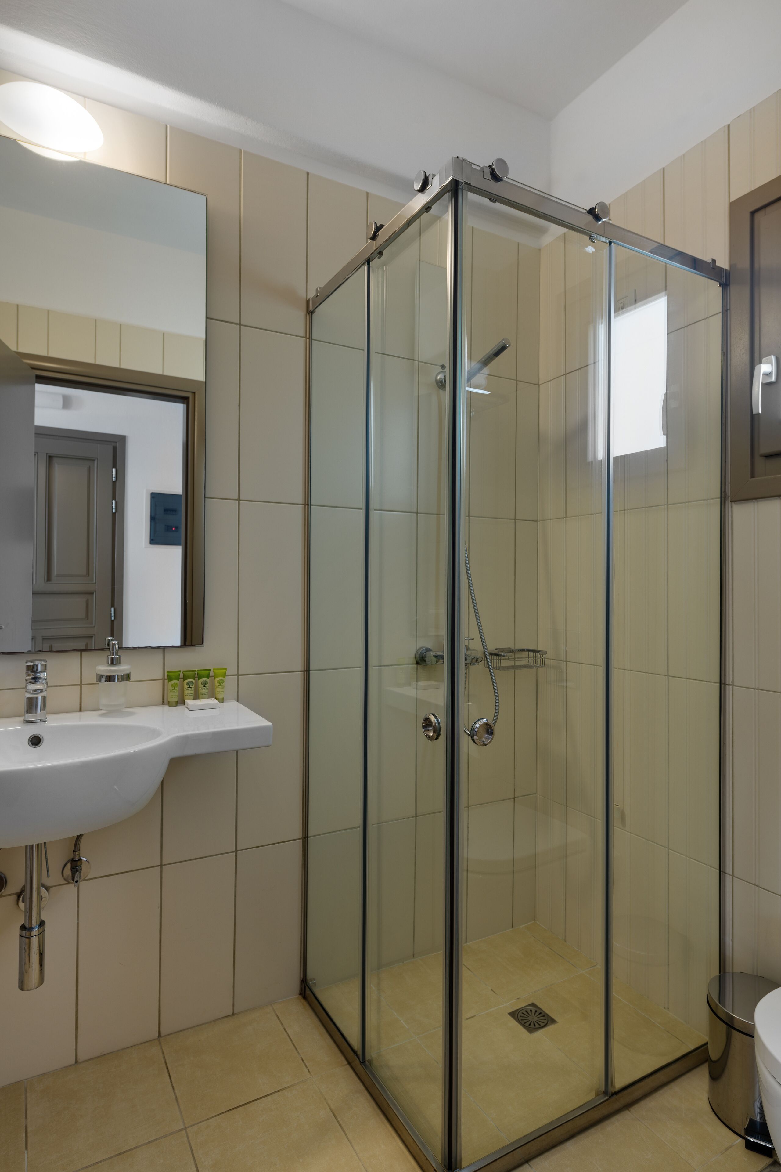 A modern bathroom with a glass-enclosed shower, a sink with a mirror, and beige tiled walls.