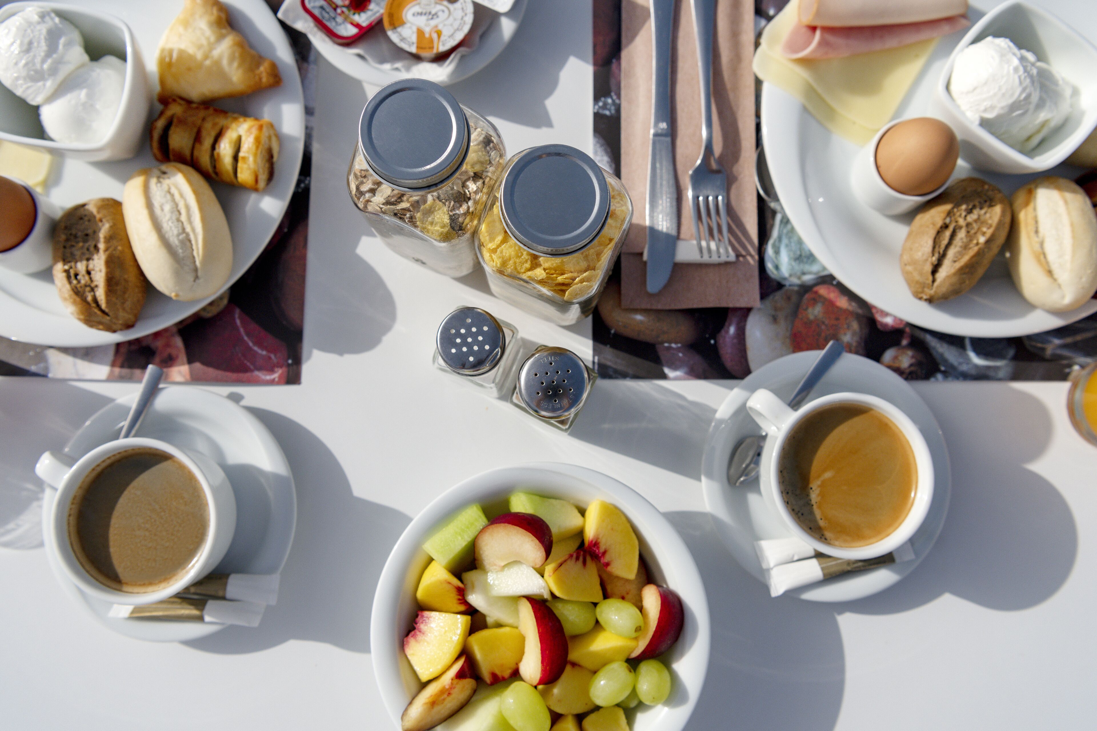 A breakfast setting with croissants, cheese, eggs, and fruit on plates, along with cups of coffee and tea.