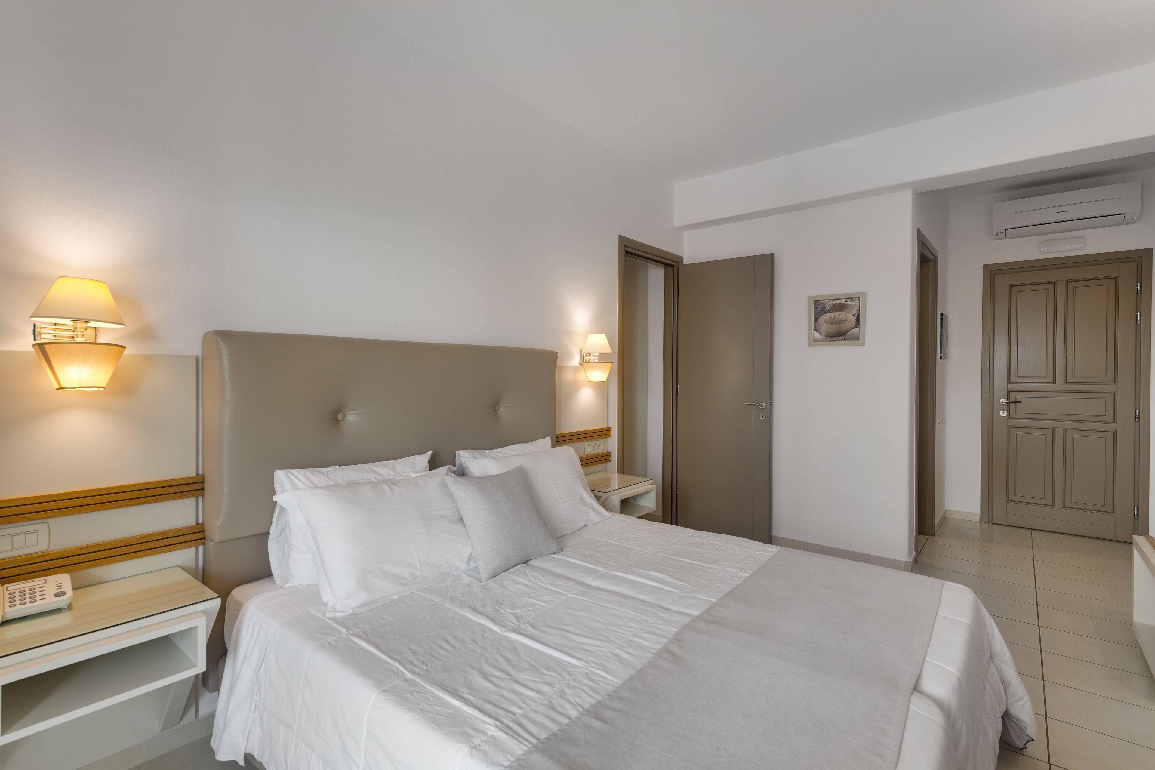 A hotel room with a large bed, bedside tables, a nightstand, and wall-mounted lamps.