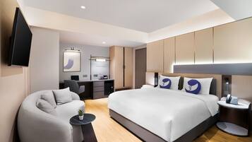 A modern hotel room with a large bed, a desk, a sofa, and a TV.