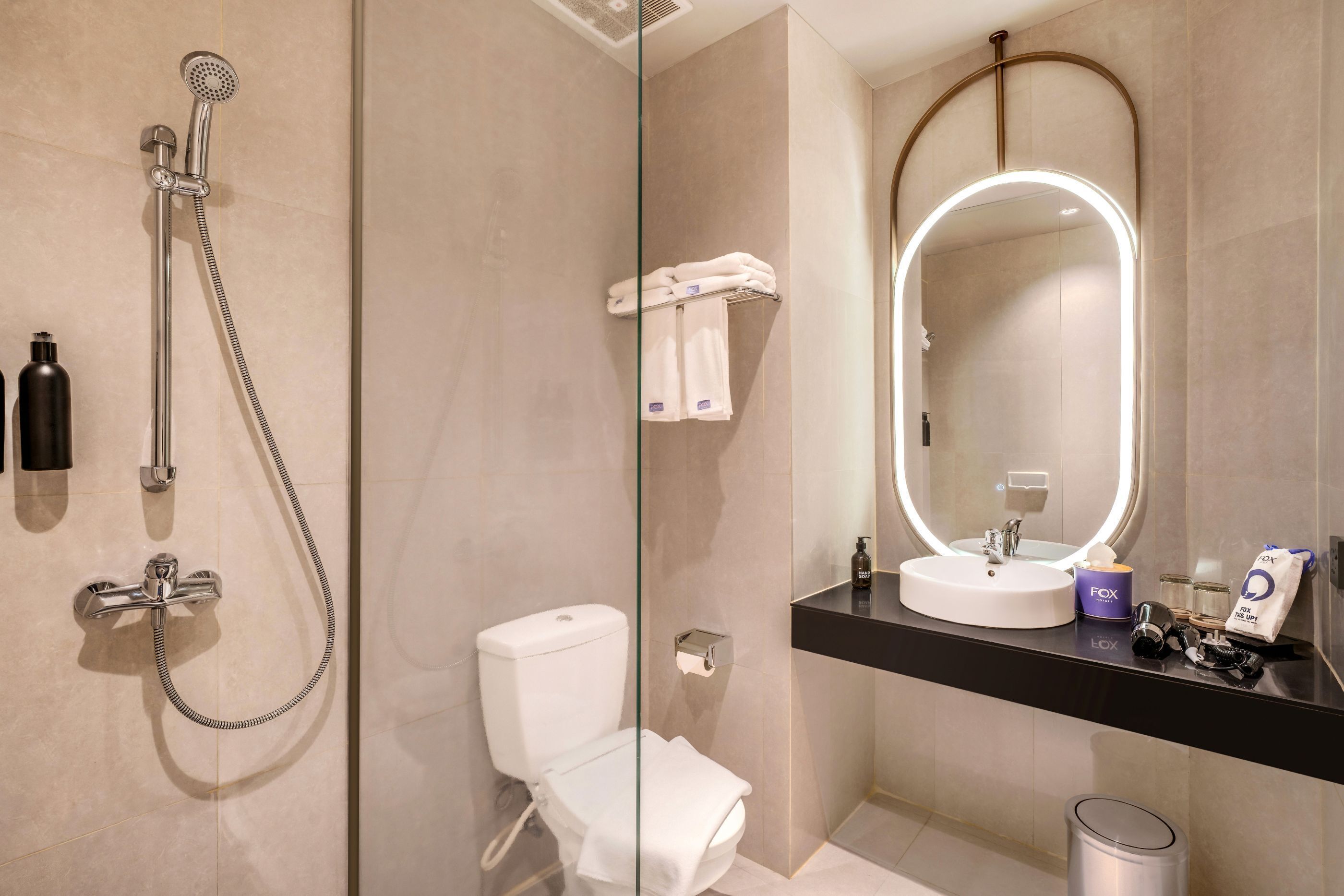 Ein modernes Badezimmer mit einer Glastrennwand-Dusche, einer Toilette, einem Waschbecken mit Spiegel und einem Mülleimer.