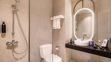 Ein modernes Badezimmer mit einer Glastrennwand-Dusche, einer Toilette, einem Waschbecken mit Spiegel und einem Mülleimer.