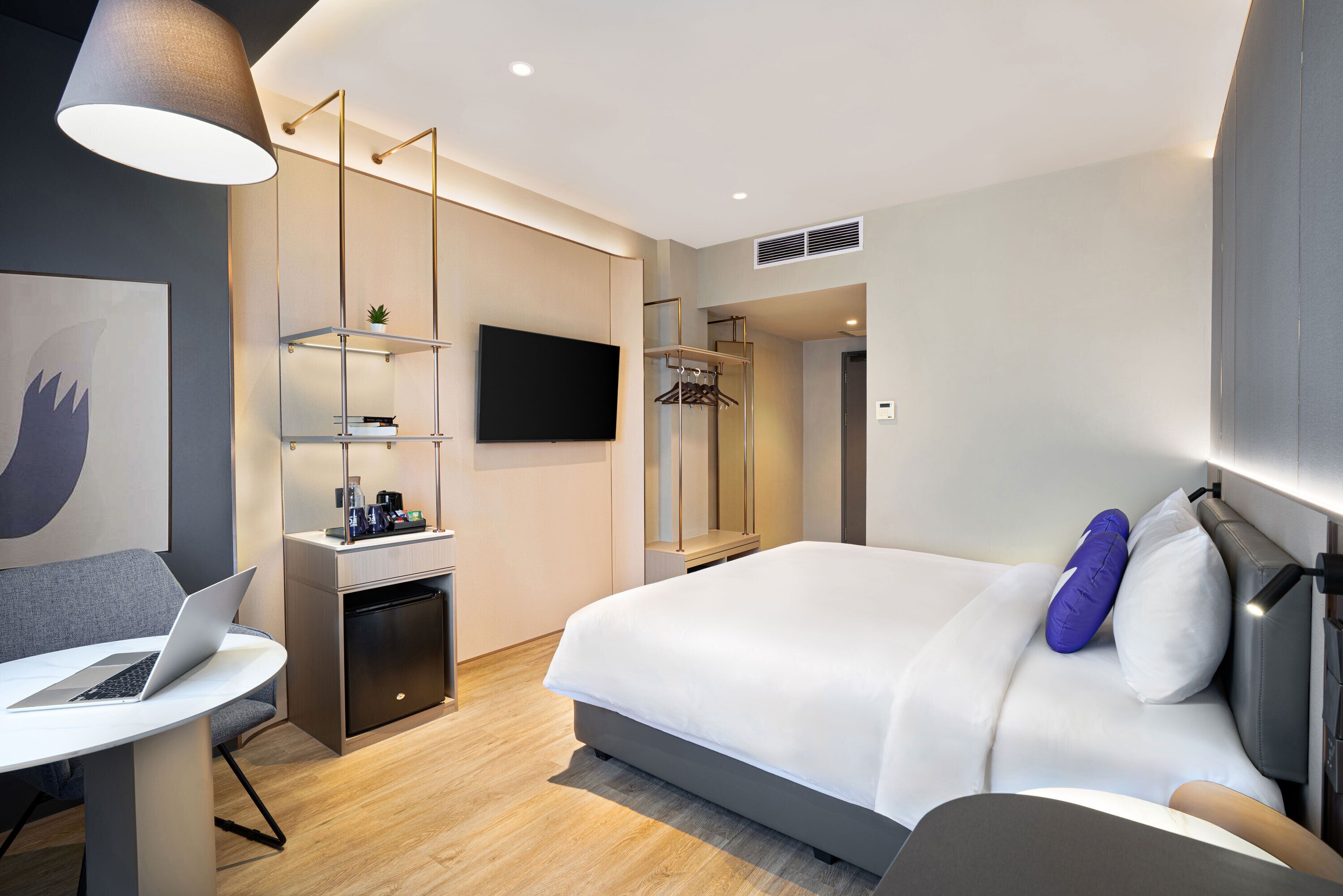 Una camera d'albergo moderna con un letto, una scrivania con un portatile, una televisione e un armadio.