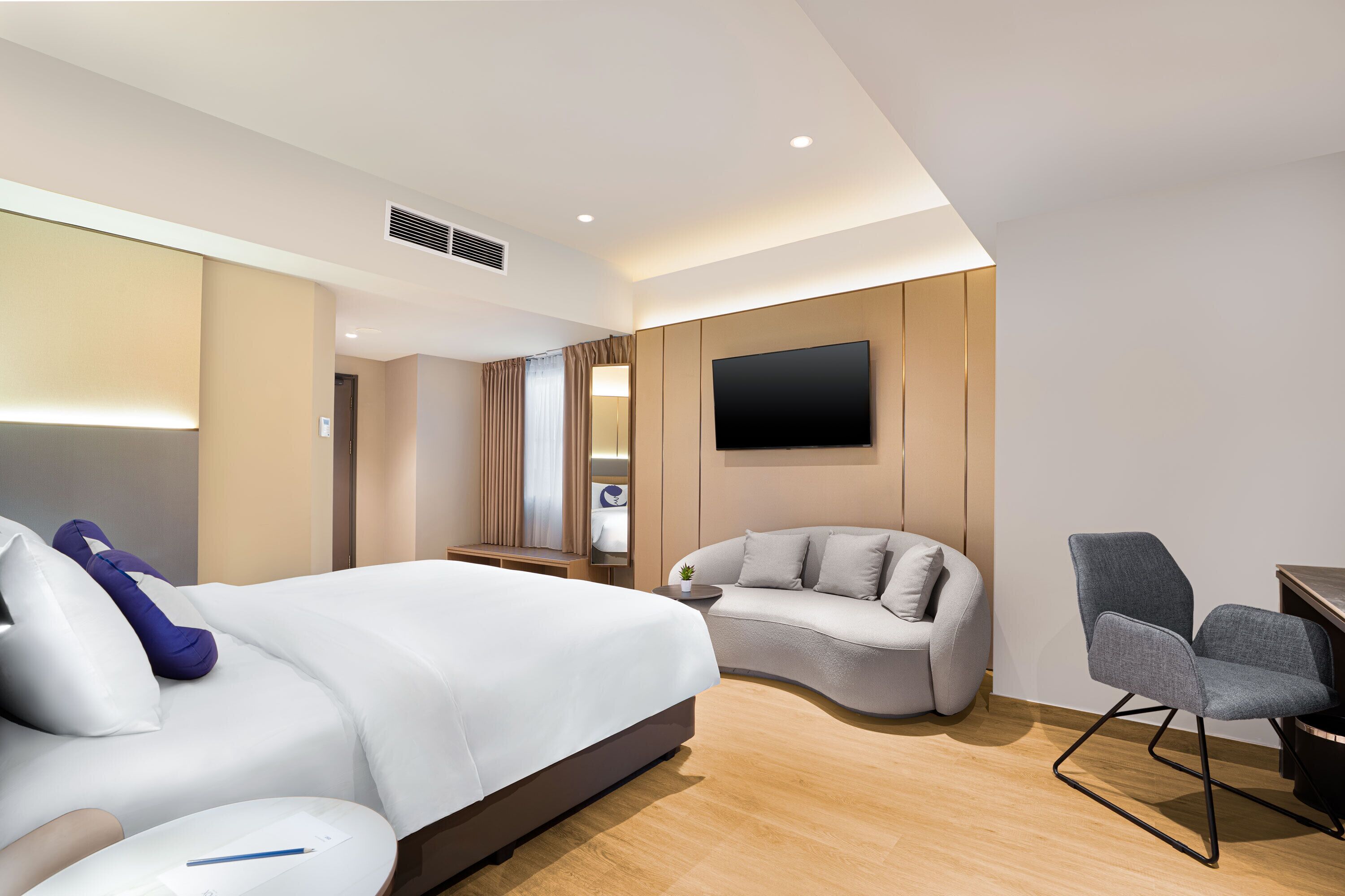 A modern hotel room with a bed, a sofa, a desk, and a TV.