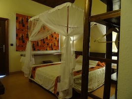 Una habitación con cama bajo un dosel, una pared con un mural decorativo y una estructura de literas de madera.