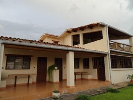 Un edificio de dos pisos con techo de tejas, múltiples ventanas y un patio cubierto con bancos.